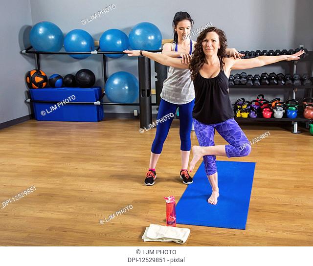 An attractive middle-aged woman doing yoga exercises at the gym with her personal trainer providing assistance; Spruce Grove, Alberta, Canada