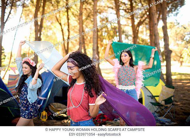 Happy young woman holding scarfs while standing on field at campsite