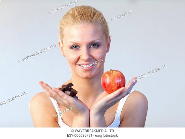 Beautiful woman holding chocolate and apple trying to decide which one to eat with focus on woman