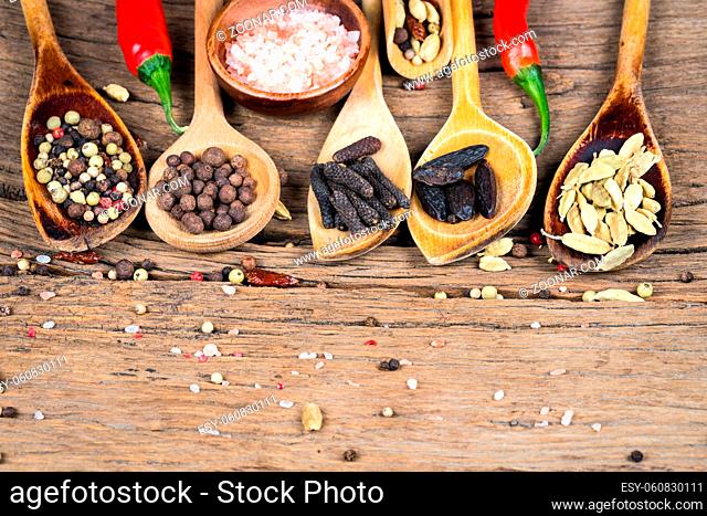 Close-up of five wooden cooking spoons with various exotic spices and two red chili peppers and a wooden bowl with pink crystal salt on a rustic wooden...