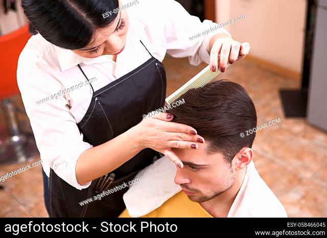 Handsome man having his hair cut by barber girl. View of hairdresser combing handsome man#39;s in hairdressing saloon