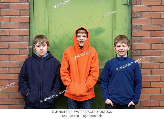 Three boys outdoors, standing against a building