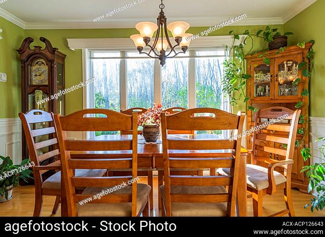 Grandfather clock, ash wood table and chairs plus buffet in dining room inside a country cottage style house, Quebec, Canada