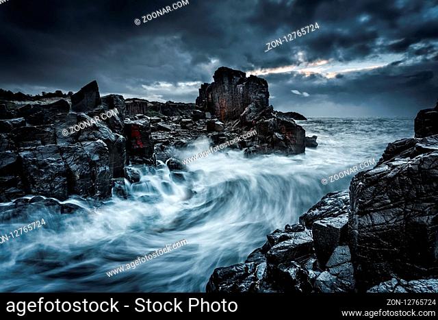 Dramatic stormy weather, rainfall, and large waves push through the rocky gully of basalt columns and wet glistening boulders on the coast of Australia