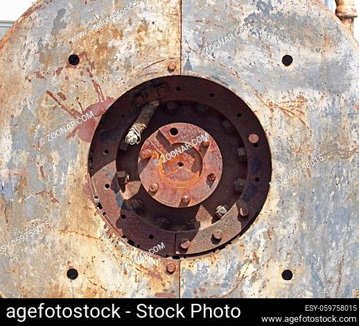 close up full frame detail of old rusting machinery with circular hole in steel plates with bolts and round drive shaft in the center in sunlight and shadow