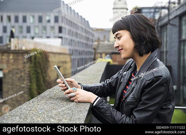 Woman on mobile phone standing at edge of building on rooftop patio