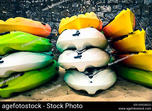 Stacked white, green and orange kayaks on a beach