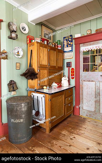 Antique wooden buffet with vintage cooking products and decorations in kitchen with worn wide pinewood plank floorboards inside an old 1835 Canadiana cottage...