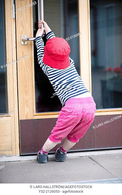 Young child struggling with heavy door, trying to open by pulling the handle