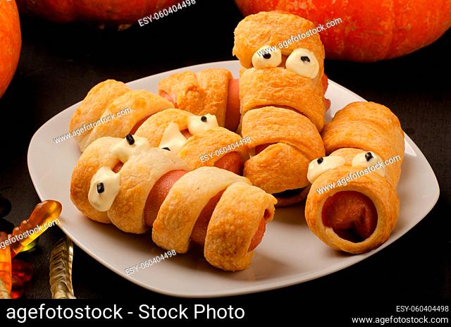 Scary sausage mummies in dough with funny eyes on table. Funny decoration. Halloween food