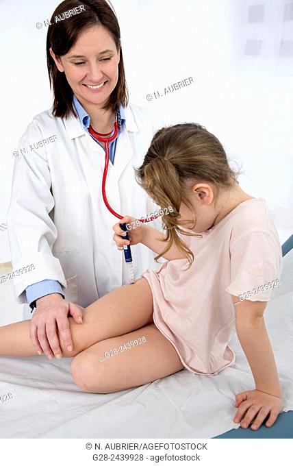 Little girl with bunches suffering from diabetes injecting herself insulin in the presence of a smiling pediatrician doctor on a medical couch in the surgery