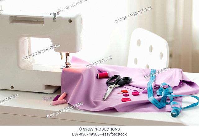 needlework, technology and tailoring concept - sewing machine with scissors, buttons, tape measure and fabric
