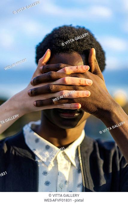 Hands covering eyes of a young black man