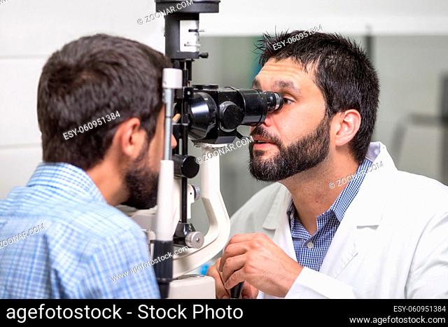 male doctor ophthalmologist is checking the eye vision of handsome young man in modern clinic. Doctor and patient in ophthalmology clinic