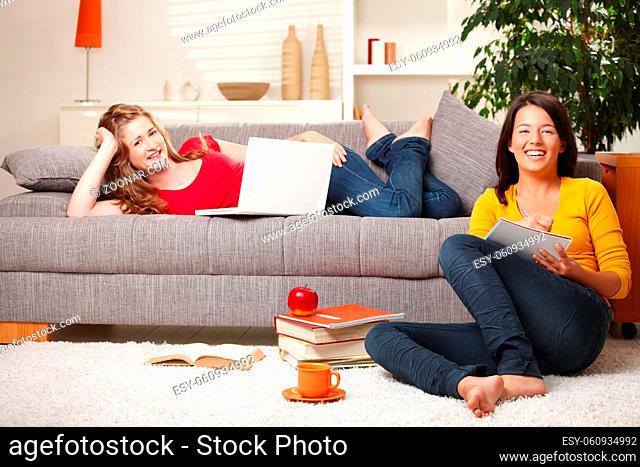 Happy schoolgirls studying together in living room with books and computer, laughing