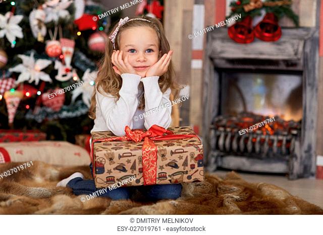 Happy pretty girl with gift box lies near Christmas tree in the room of the house. Merry Christmas and New Year