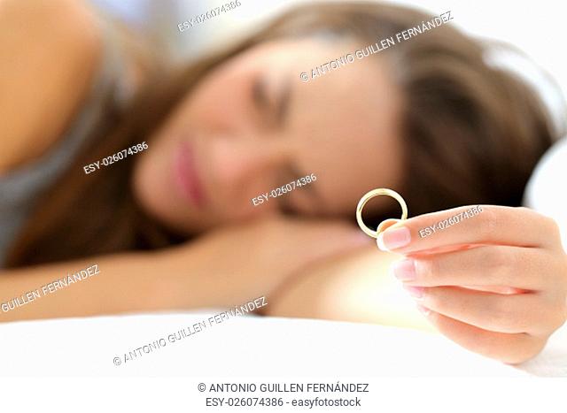 Sad wife mourning after divorce holding a wedding ring lying on the bed