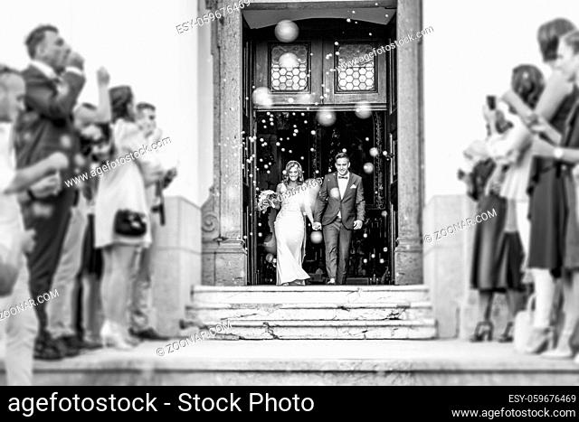 Newlyweds exiting the church after the wedding ceremony, family and friends celebrating their love with the shower of soap bubbles