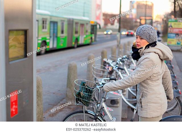 Lady dialing on keyboard of urban bicycle station. Bikes for rent. Green sustainable ecological public transport. Healthy lifestyle