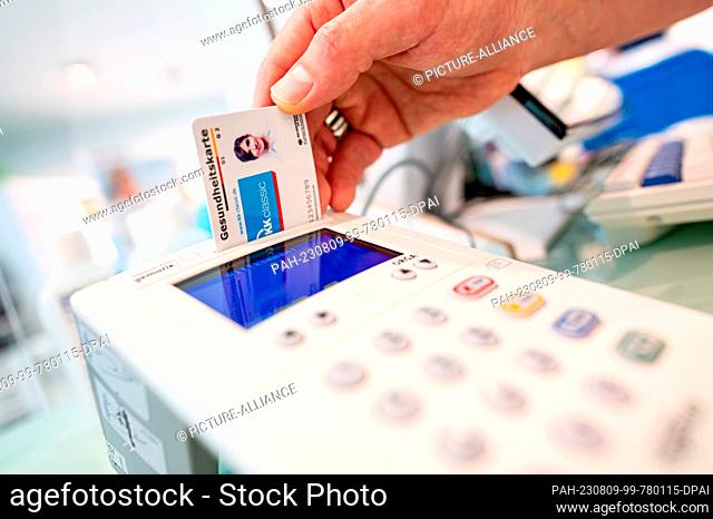 09 August 2023, Berlin: A pharmacy employee inserts a health card into a reader. Photo: Fabian Sommer/dpa. - Berlin/Berlin/Germany