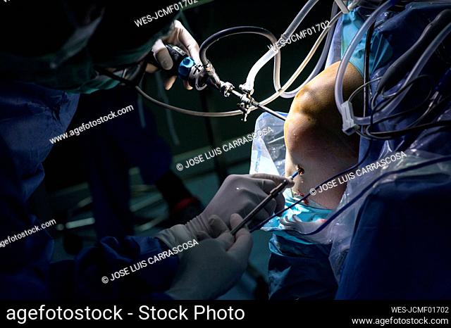 Male orthopedic surgeon performing operation on patient knee in ICU
