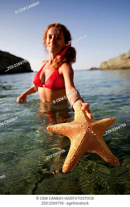 Woman in the sea with a starfish in her hand at Agios Georgios beach, Folegandros, Cyclades Islands, Greek Islands; Greece, Europe
