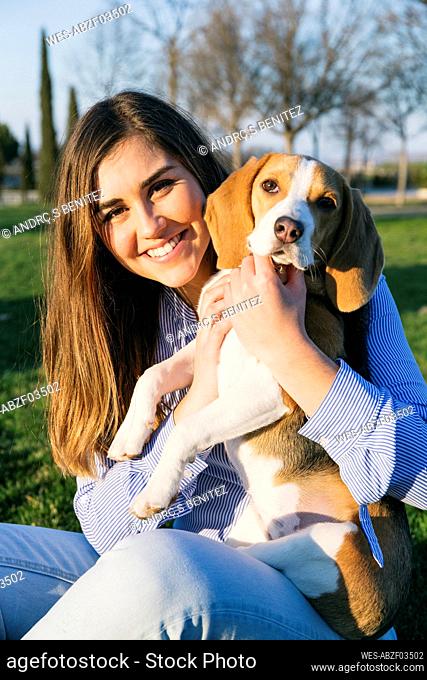 Mid adult woman sitting with dog at park during sunset
