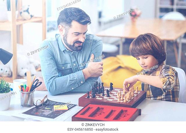 Men's club. Bearded father sitting at a desk with his concentrated little son playing chess at home