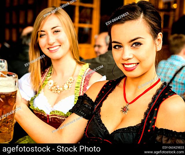 Girls in traditional Dirndl dress, one a blend between Asian and Caucasian, one Caucasian are drinking beer and having fun at the Oktoberfest