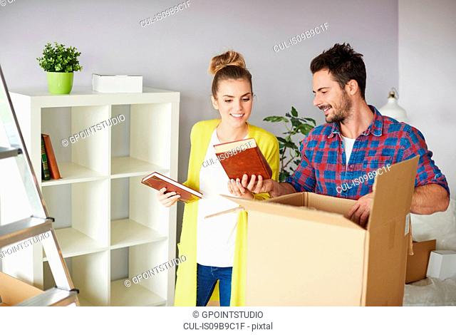 Young couple moving home, packing belongings into cardboard box