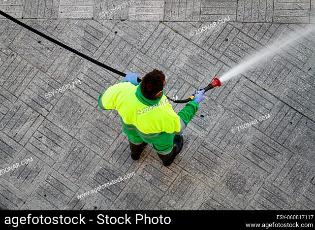 Worker holding a hose cleaning the sidewalk with water. Urban Maintenance or cleaning concept