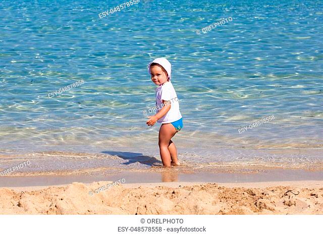 Little child girl is playing on sandy beach near blue sea