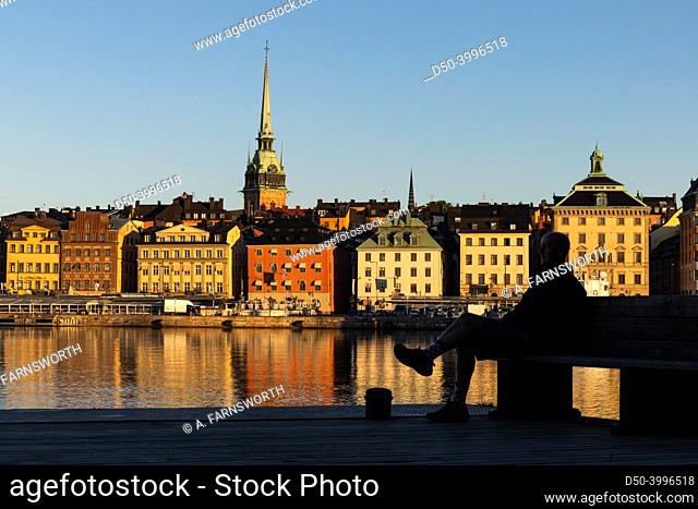 Stockholm, Sweden A man sits on a bench on Skeppsholmen with a view over water and Gamla Stan, or Old Town