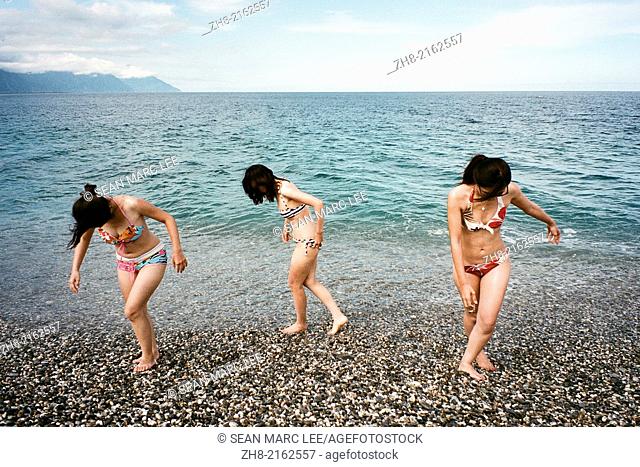 Three young woman in swimsuits dancing on a rocky beach in Taiwan