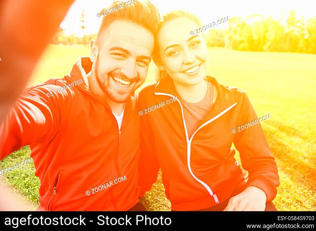 Closeup portrait of sport man and woman making selfies in green park or forest while sitting on green grass and resting after jogging. Toned