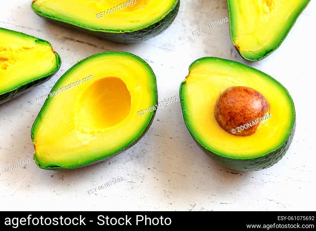 Halved avocado fruits closeup with green yellow pulp, brown seeds visible on white working board