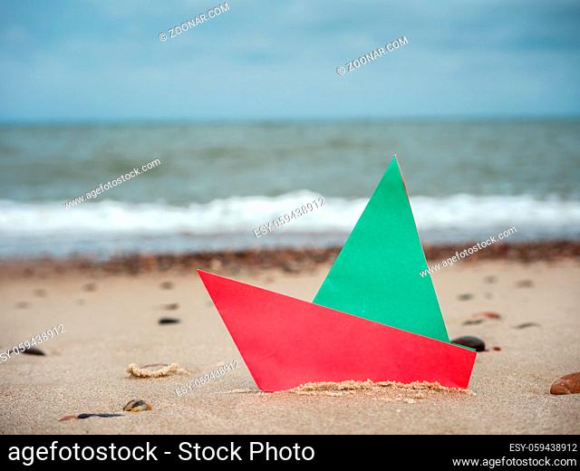 Red and green paper boat on the beach sand against the sea
