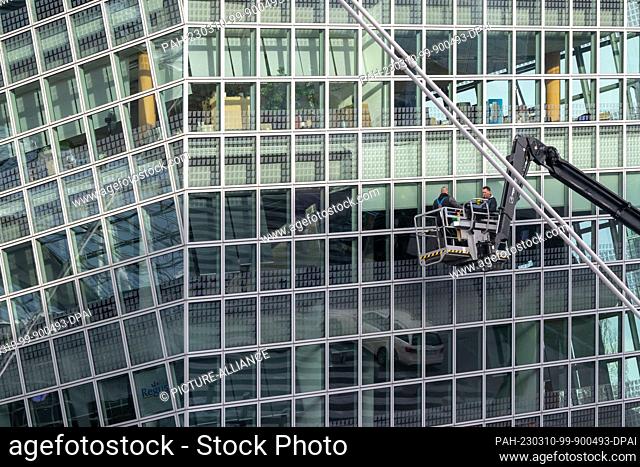 10 March 2023, Bavaria, Munich: Two men on a lifting platform clean the windows of a high-rise building at Munich Airport. Photo: Peter Kneffel/dpa