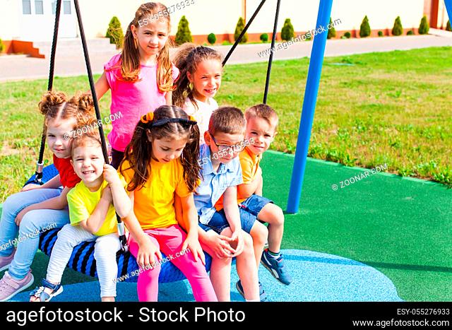 Obedient children sit on a spider web nest swing on a playground near a kindergarten on a wonderful summer day
