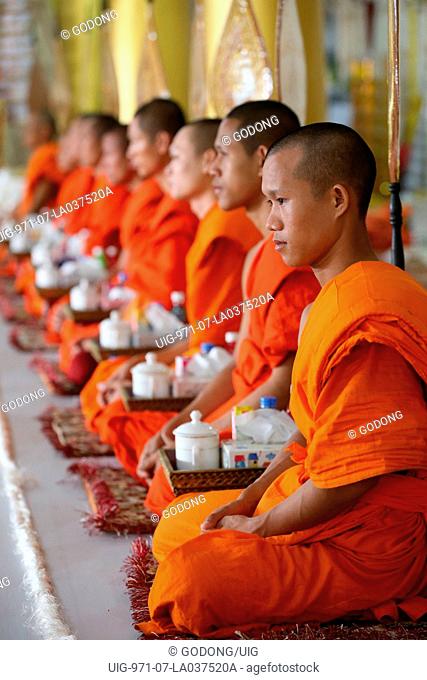 Seated Buddhist monks chanting and reading prayers at a ceremony