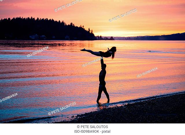Couple practising yoga on beach at sunset