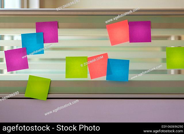 Randomly scattered colored sticky notes over glass screen of a bench desk