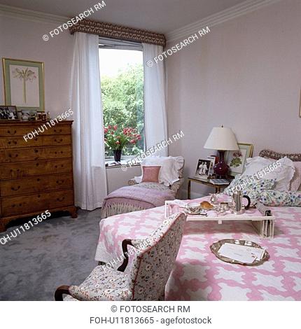 Breakfast tray and pink patchwork quilt on bed in traditional white country bedroom with white voile curtains on window