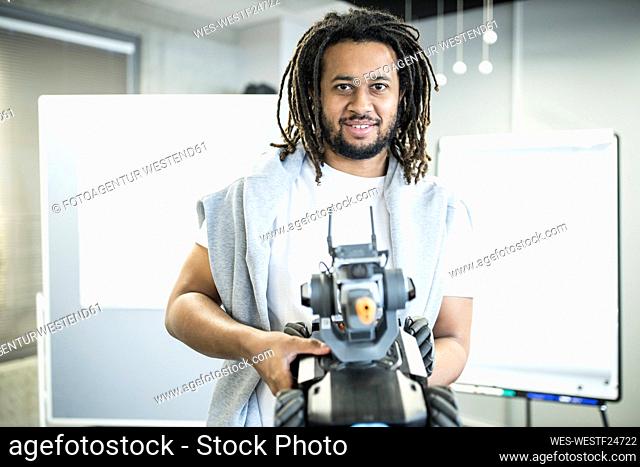 Smiling technician holding robotic combat tank at workshop