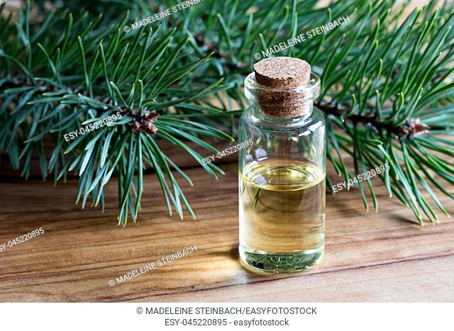 A bottle of pine essential oil on a wooden table with pine branches in the background