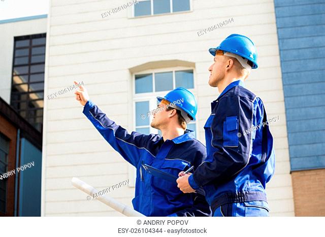 Male architect showing something to colleague while holding blueprint outdoors