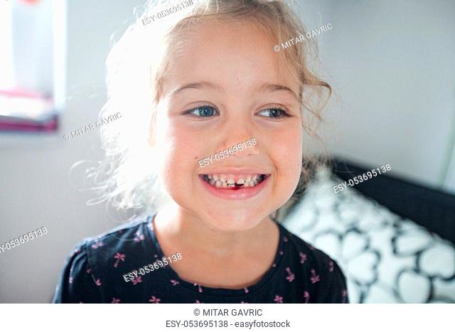 Portrait of cute smiling little girl showing dropped first milk tooth at home