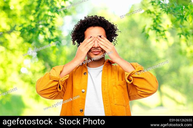 man closing eyes by hands on natural background