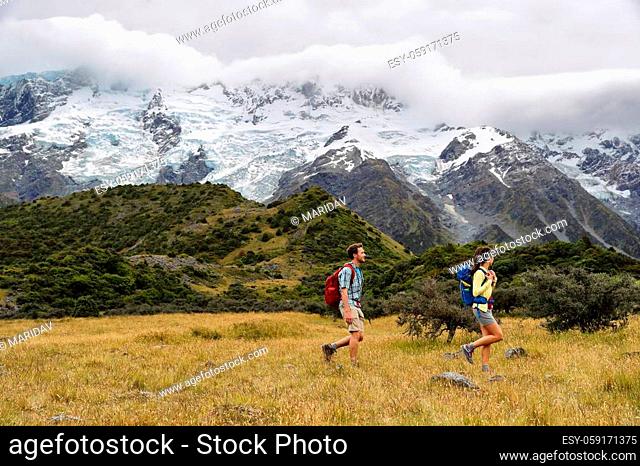New Zealand travel hikers hiking on snow capped mountains landscape background. Couple trampers walking on Hooker Valley Track