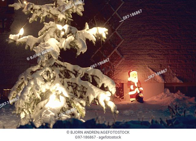 Snow covered Christmas tree and lighted plastic Santa Claus. Sweden